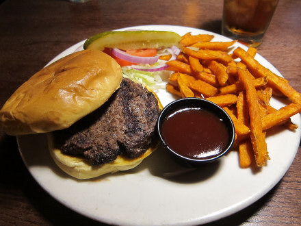 Old fashioned burger with toppings on the side and barbecue sauce added