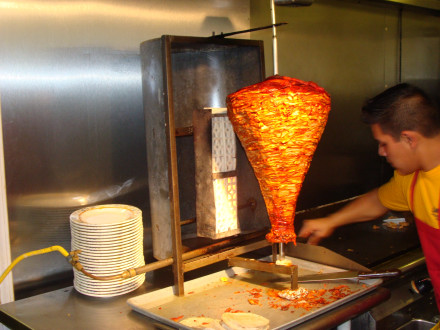 Meat for tacos al pastor being sliced off from the rotisserie